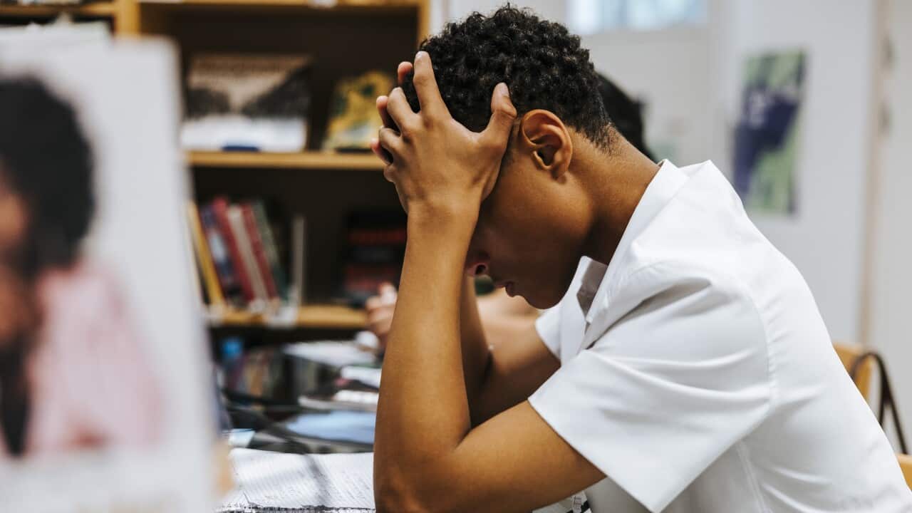 Side view of stressed teenage boy sitting with head in hand at library of school