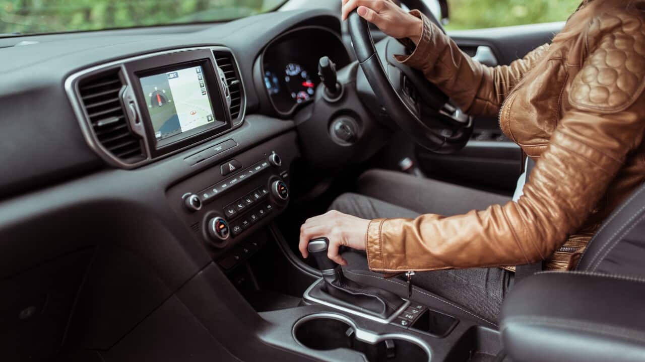 Close-up, woman driving a car includes a gearbox, reversing, starting to move in woods, leather jacket, automatic transmission. Touch screen navigation map app on monitor.