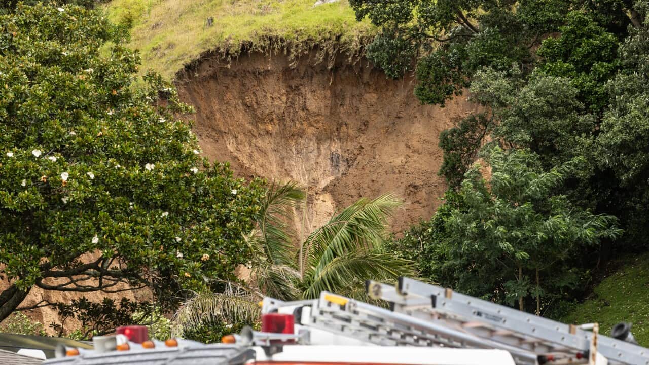 A cavernous gap in a muddy hillside, with emergency vehicles nearby.