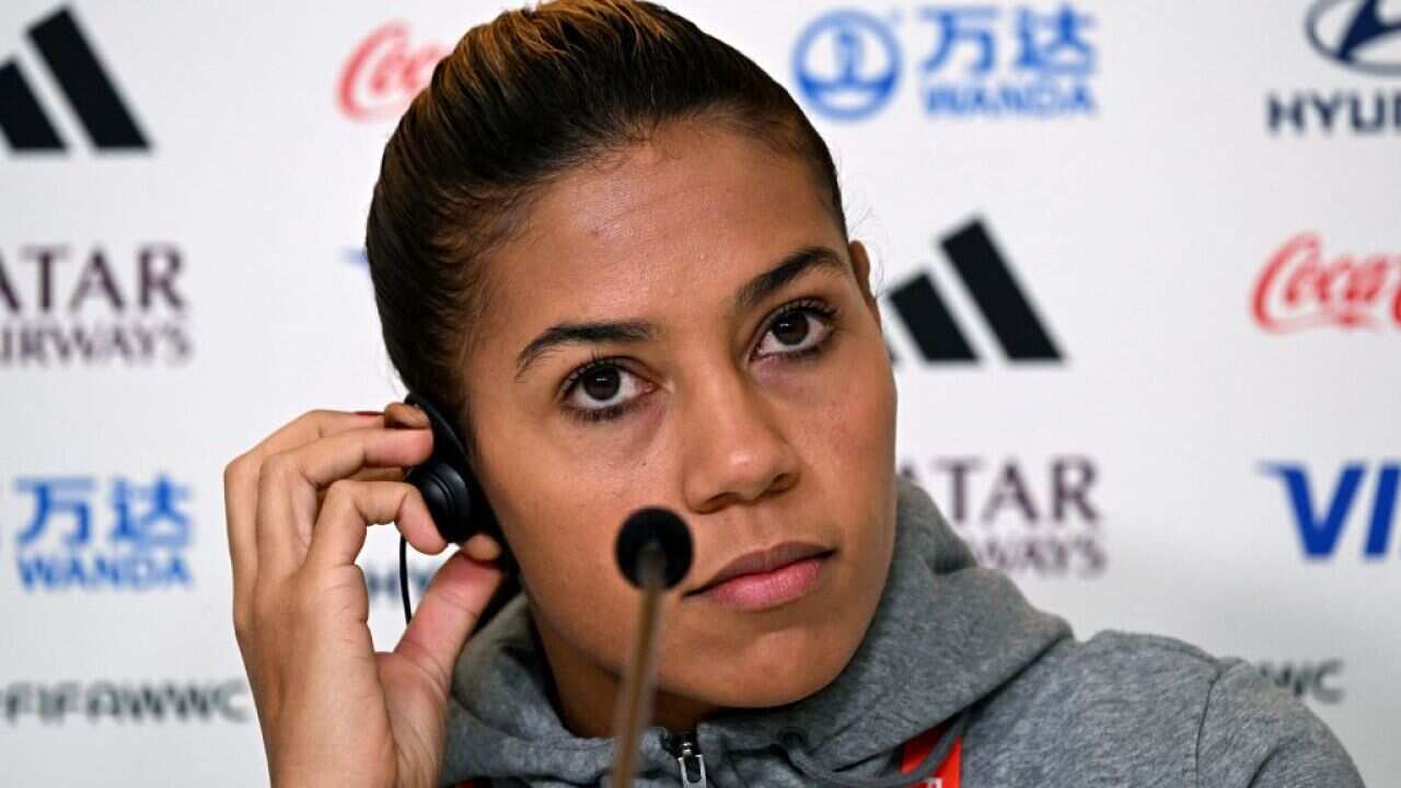 A woman in a grey hoodie holding an earpiece in her ear.