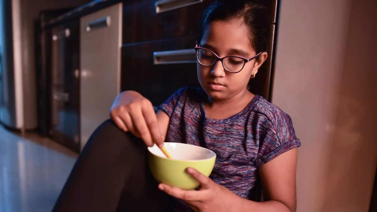 Girl eating from bowl while sitting on kitchen floor