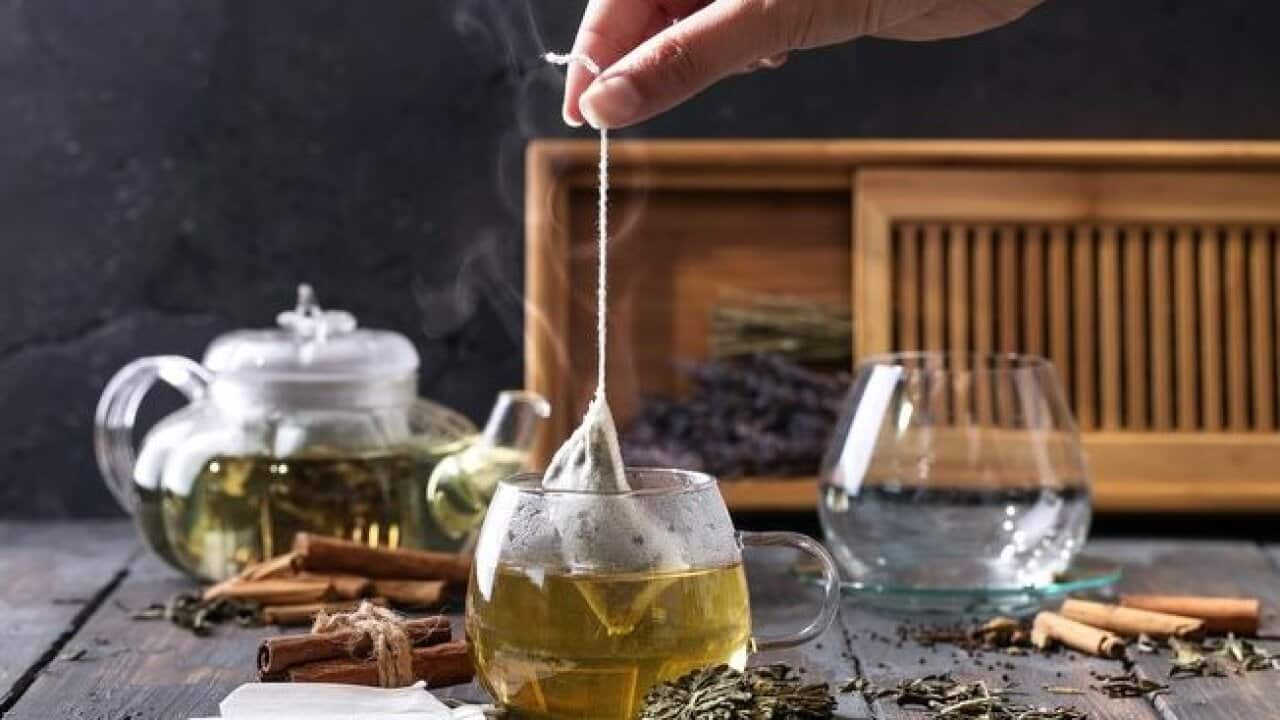 Tea bag being brewed in cup, spices and leaves around it