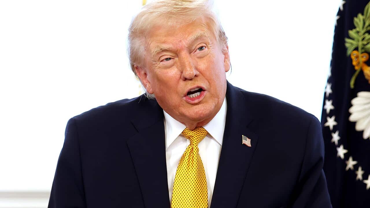 Donald Trump, wearing a dark suit and a yellow tie, is speaking.