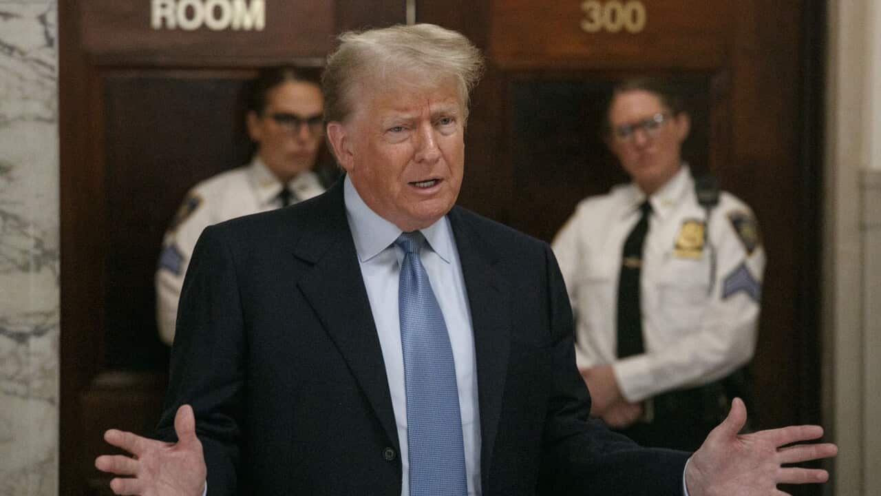 Donald Trump in the foreground as two security officials look on in the background.