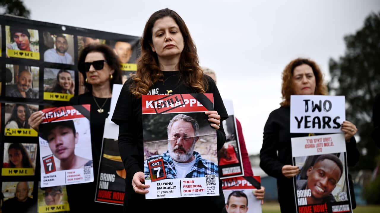 A group of women stands outdoors holding signs featuring photographs of people who are still held hostage in Gaza.
