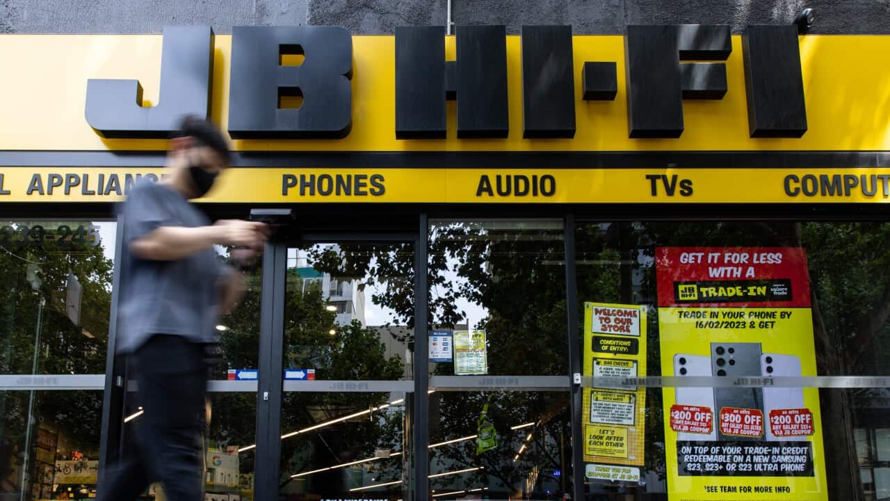 A man walking past the entrance of a JB Hi-Fi store.