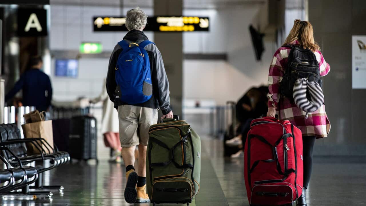 A man and woman carrying suitcases walking away from the camera in an airport.