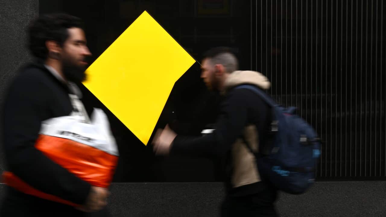 People walk past a yellow logo.