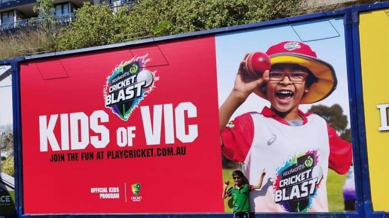 Rishaan Khandelwal posing with a 'Cricket Blast' hoarding in Melbourne