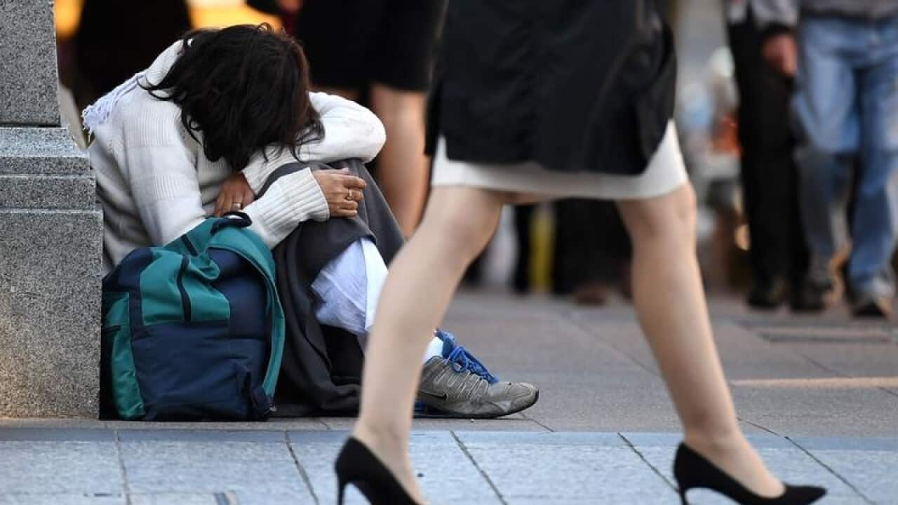 A homeless woman sits on a street corner