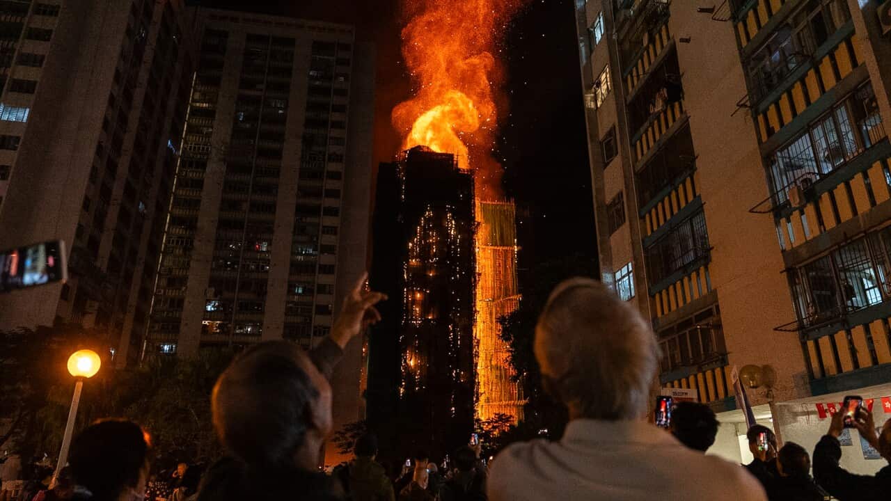 People on the ground looking up and watching as a building is engulfed in flames.