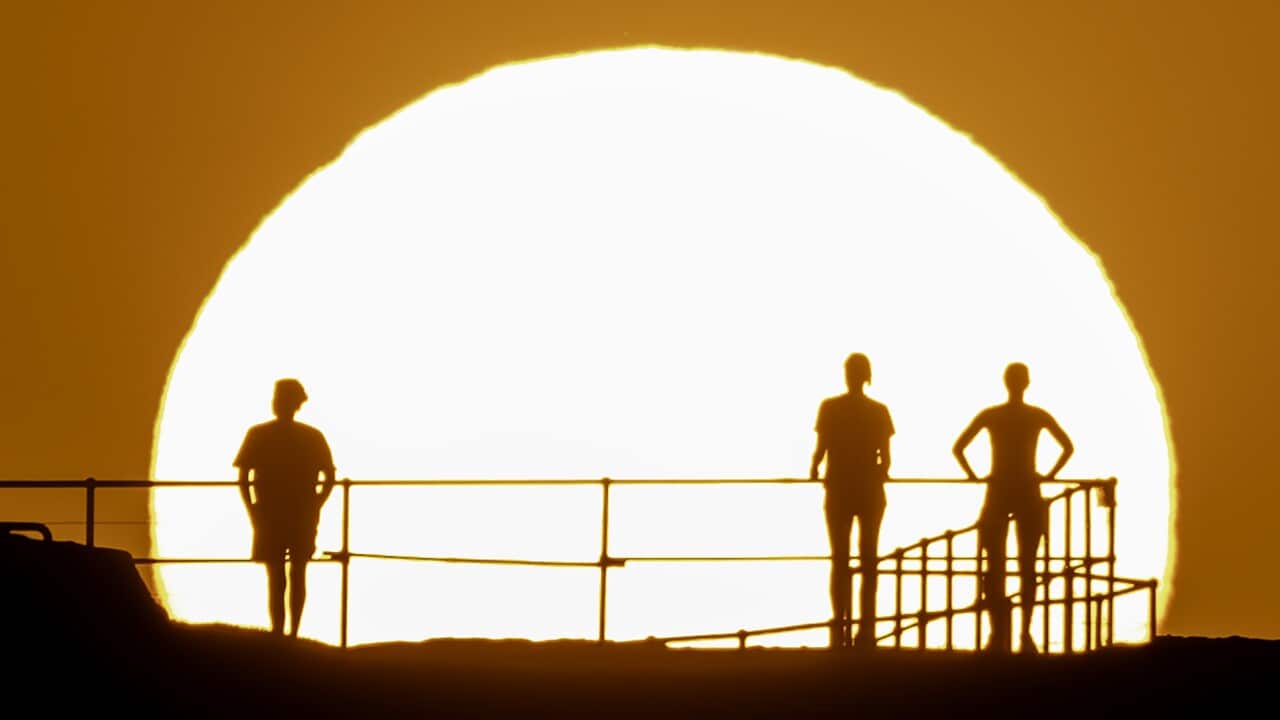 Silhouettes of people standing on an outlook, with a hot sun in the background.