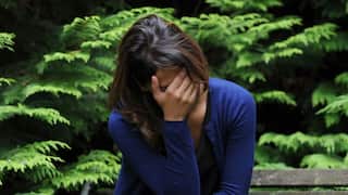 A woman sitting on a bench in a park with her head in her hand