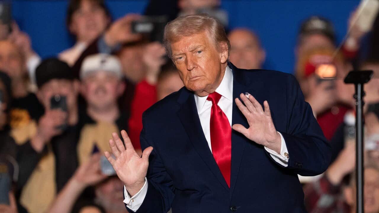 President Trump speaking at an event with both hands raised, palms towards the crowd with a serious look on his face