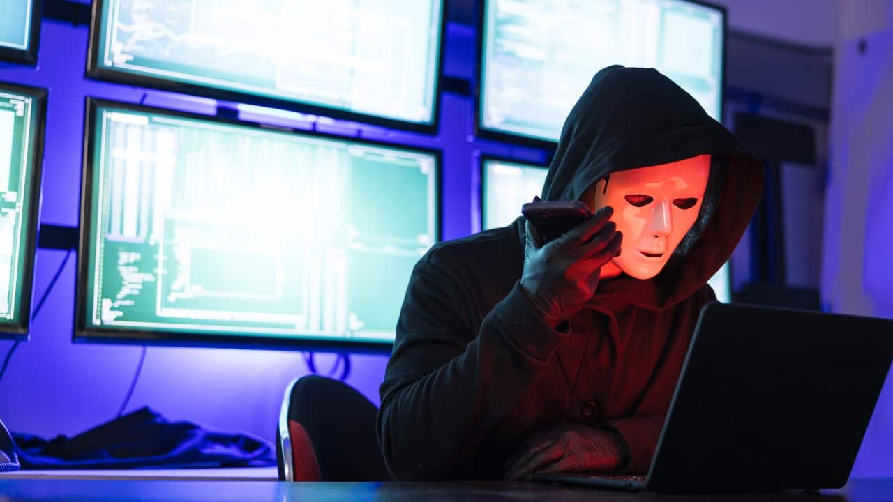 Hacker Wearing Mask using laptop computer for cyber attack and calling on cellphone, Data thief, internet attack, darknet and cyber security concept
