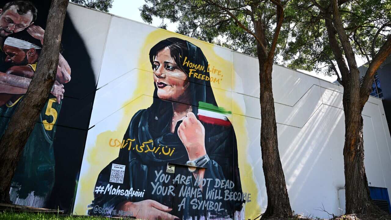 A mural of Mahsa Amini on a wall surrounded by trees and grass