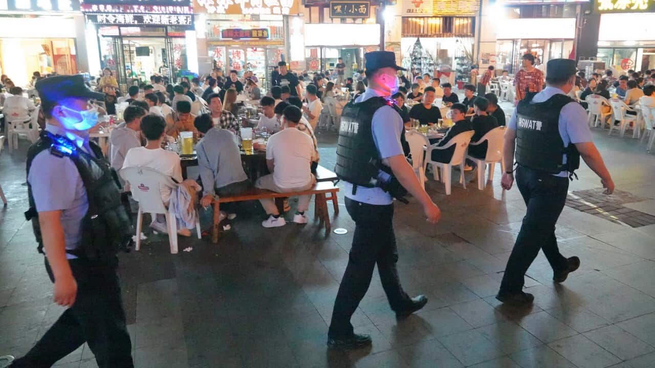 Chinese police officers walk through a busy night market, where people are dining.