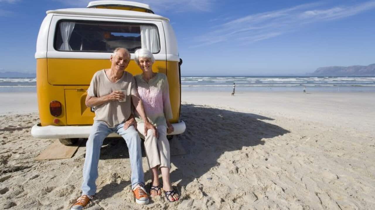Senior couple sitting on back of camper van on beach, smiling, portrait