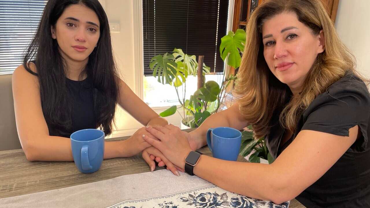 A mother and daughter hold hands while sitting at a table.