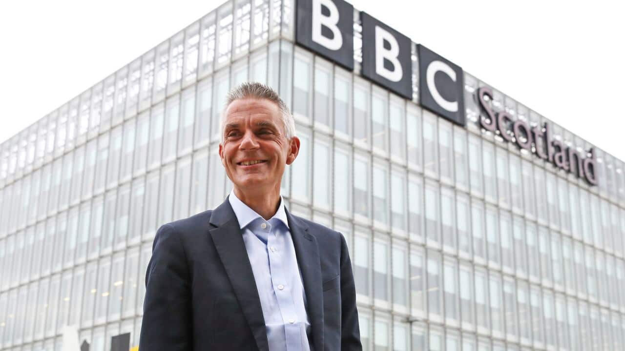 A man in a suit stands in front of a building with a sign that reads 'BBC Scotland'