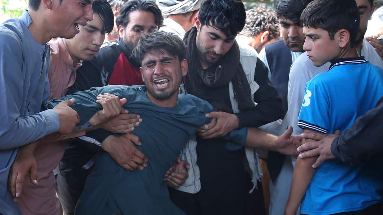 A relative wails near the coffins of victims of the wedding hall bombing in Kabul