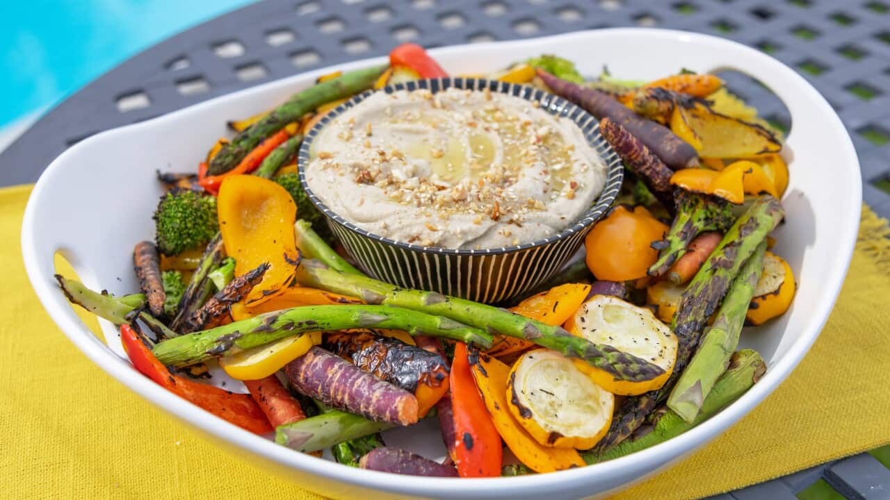 In a wide white bowl holds a colourful array of grilled vegetables and a small striped bowl filled with creamy dip.
