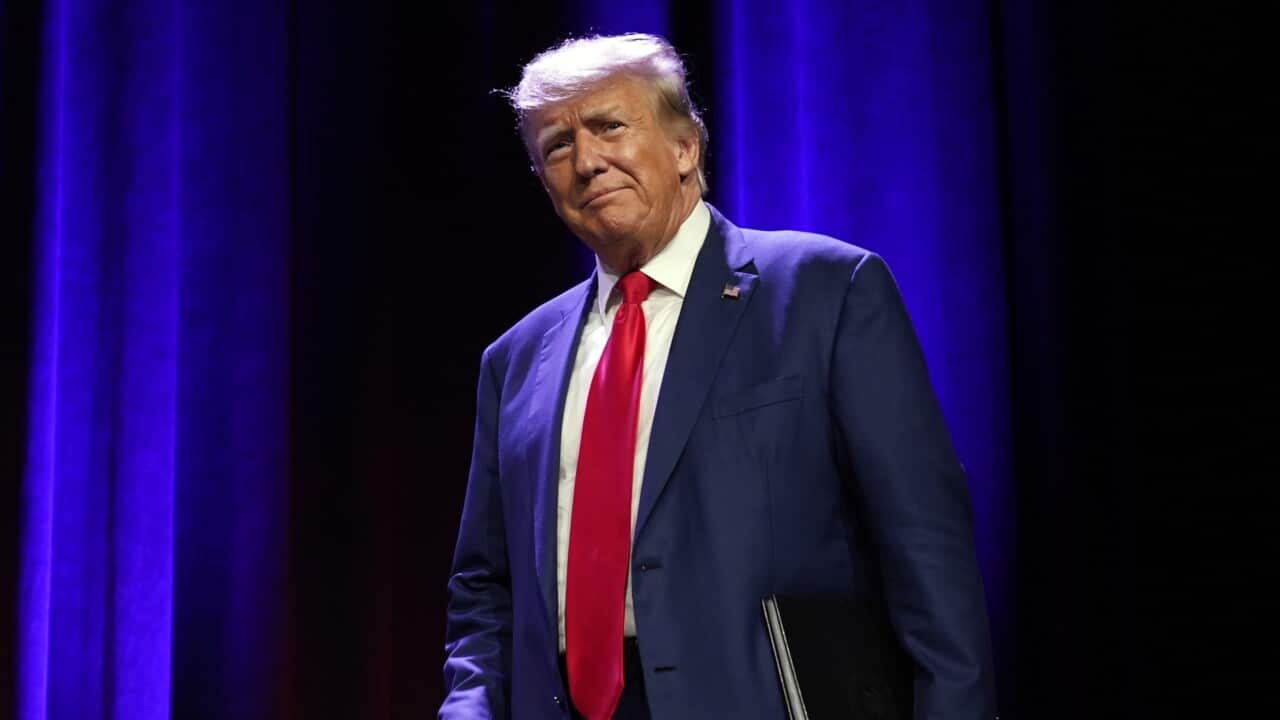 Wearing a dark blue suit and red tie, Donald Trump  walks across a stage