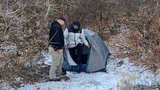 Kai Zhuang emerges from a tent surrounded by snow and trees.