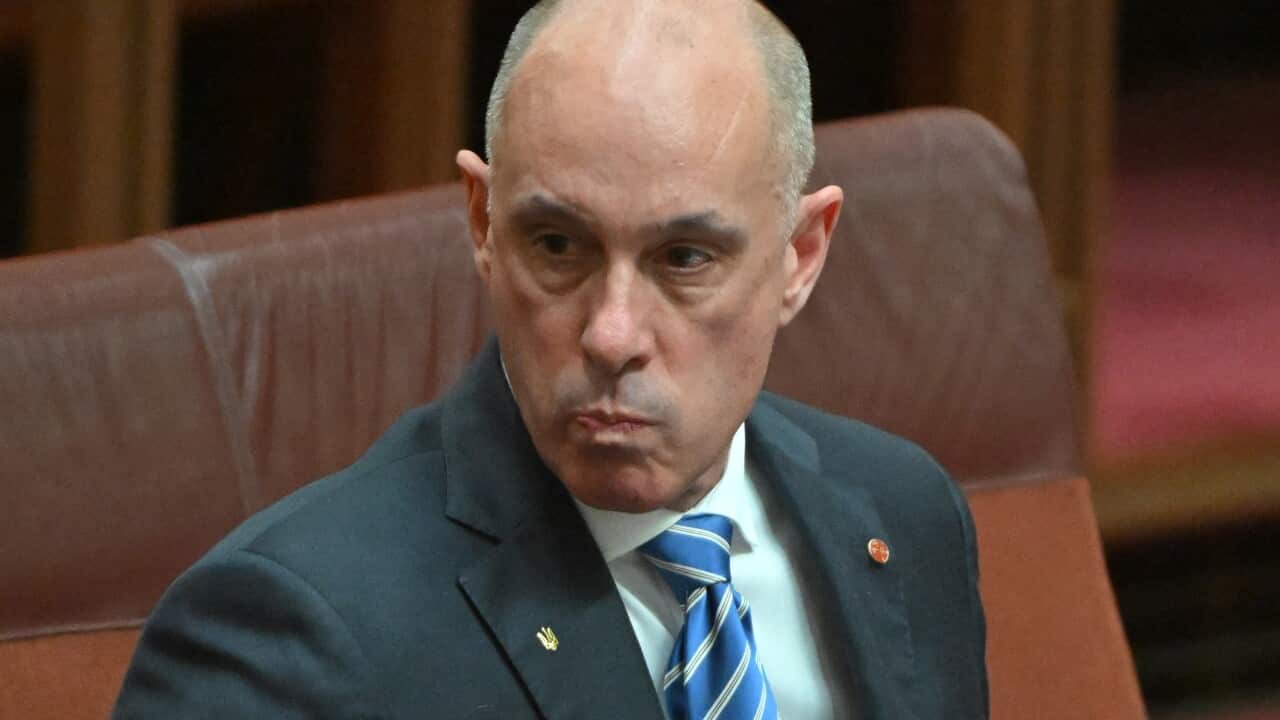 A man seated at a desk in front of a microphone.
