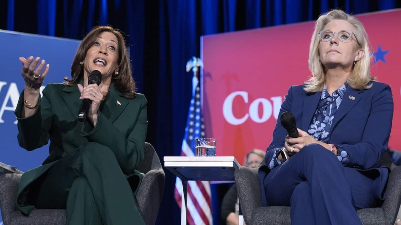 Two women seated on stage as one speaks.