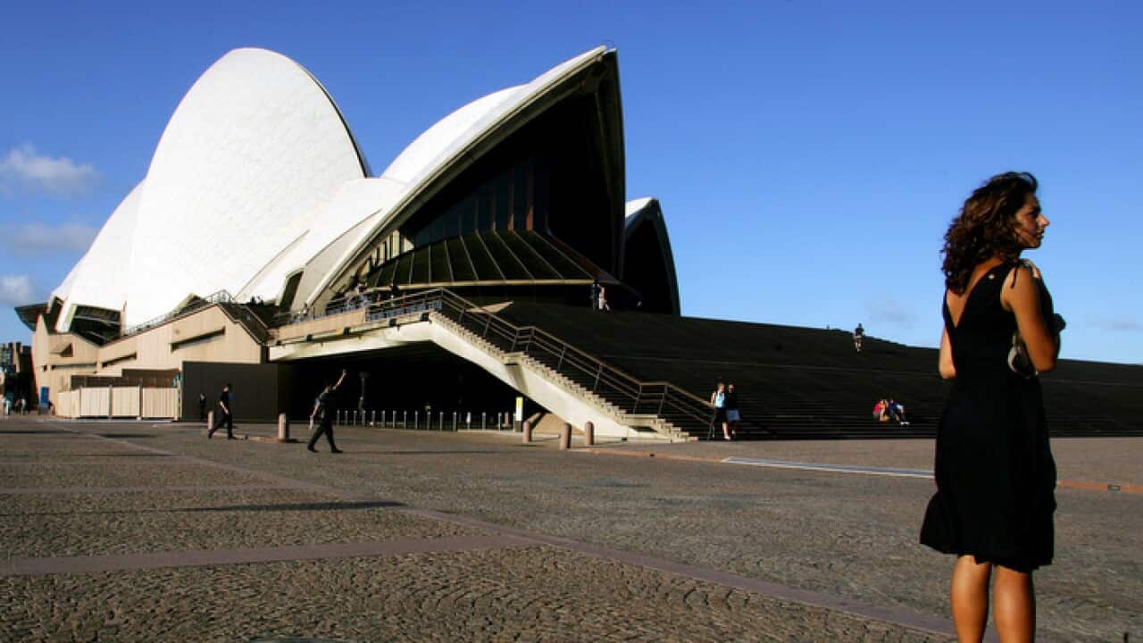 A tourist stands on a path leading toward the Sydney Opera House and a construction barricade in Sydney, Australia.