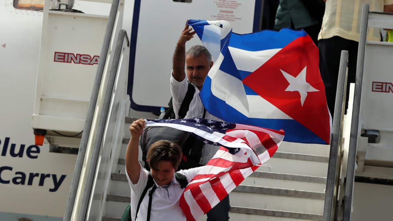 People waving Cuban and US national flags disembark from a plane