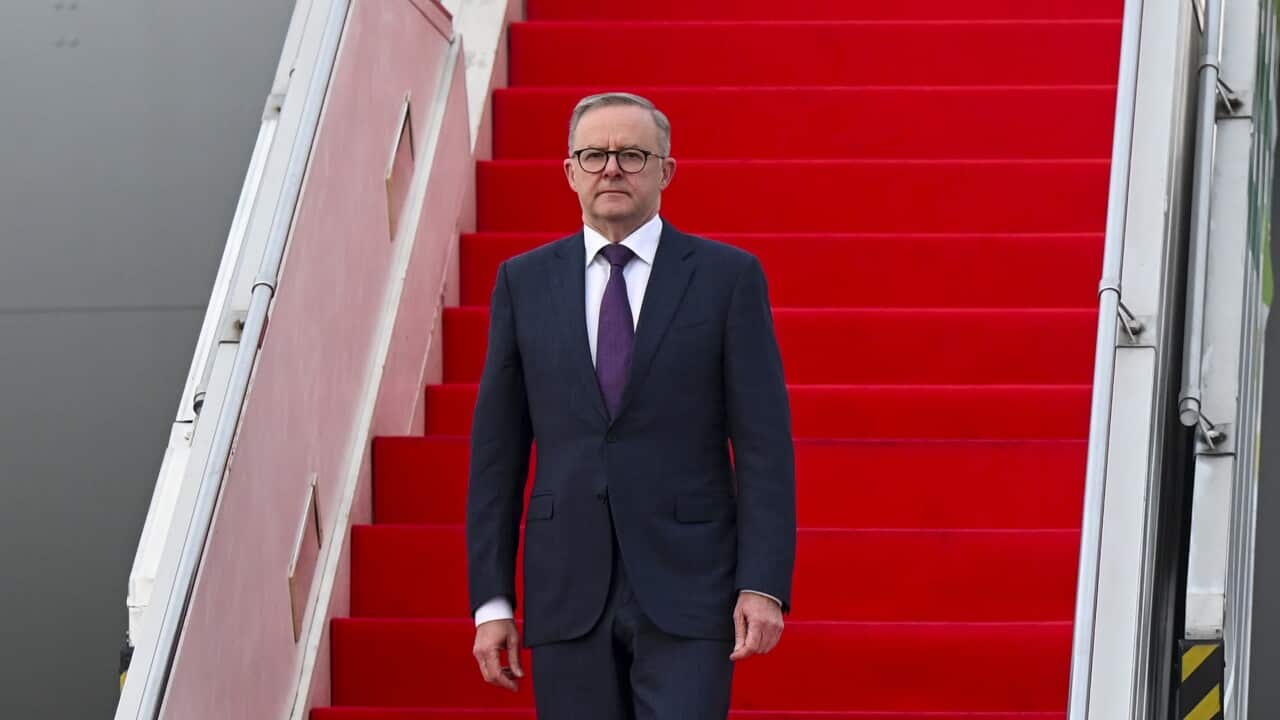 Australian Prime Minister Anthony Albanese walks down red stairs of the plane on arrival in Jakarta wearing a suit. Guards supervise his exit on the side.
