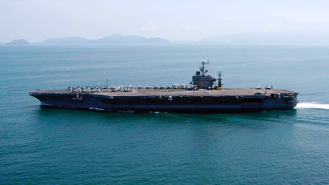 A US aircraft carrier sailing in the ocean, islands can be seen in the background