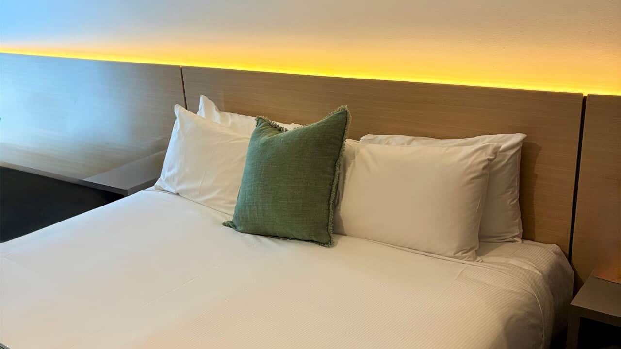 A hotel bed neatly made with white sheets and a green cushion.