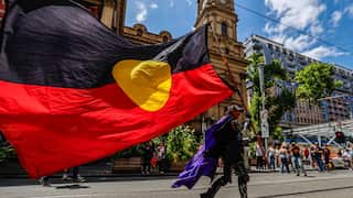 A man holding a large Aboriginal flag as he walks down a city street during a protest