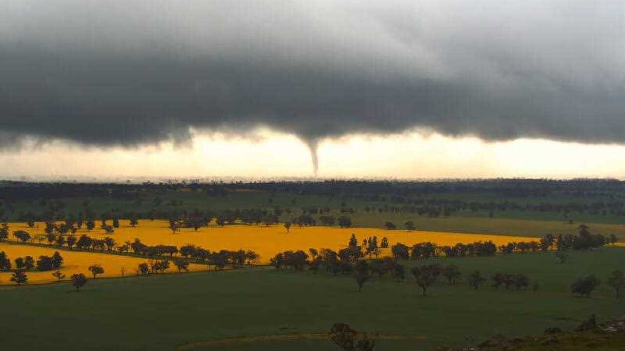 Funnel cloud forming over farmland with dark storm clouds above.