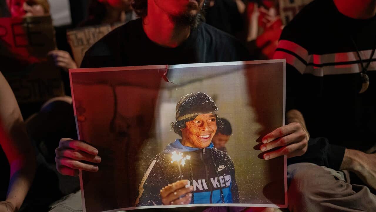 A person holds up a large photograph of a smiling young man holding a sparkler during a nighttime protest or vigil.