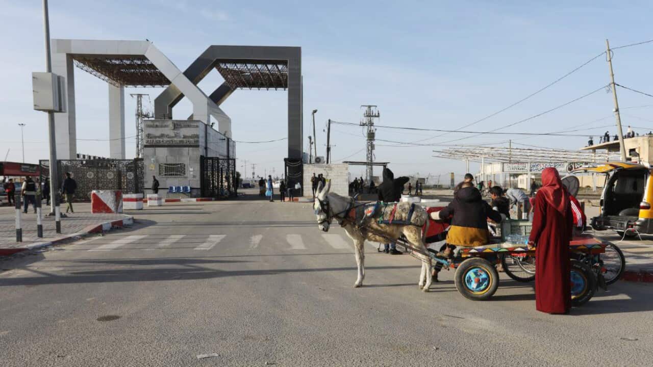 People and vehicles on a road near a border crossing.