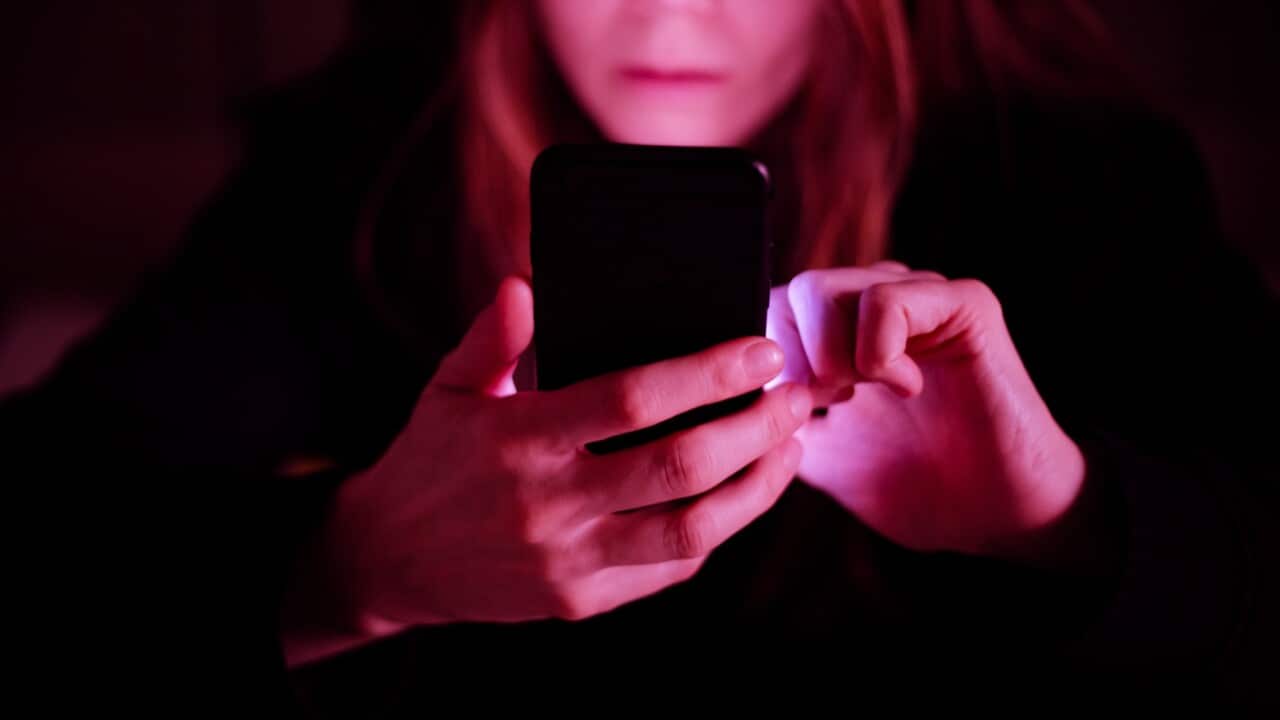A woman using mobile phone at night, under colorful LED lights at a pub / bar