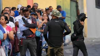 Armed men monitor people lining up outside a supermarket