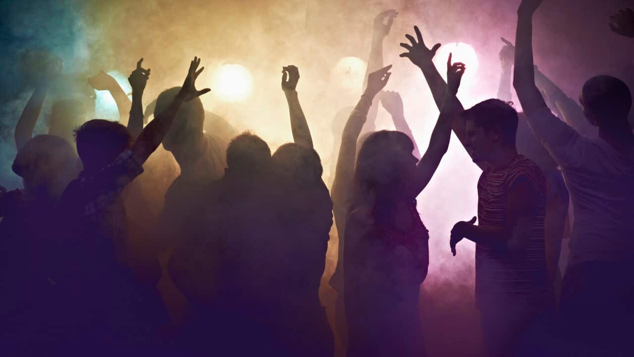 Multitud de personas en un concierto agitando sus brazos en alto, rodeados de humo colorido.