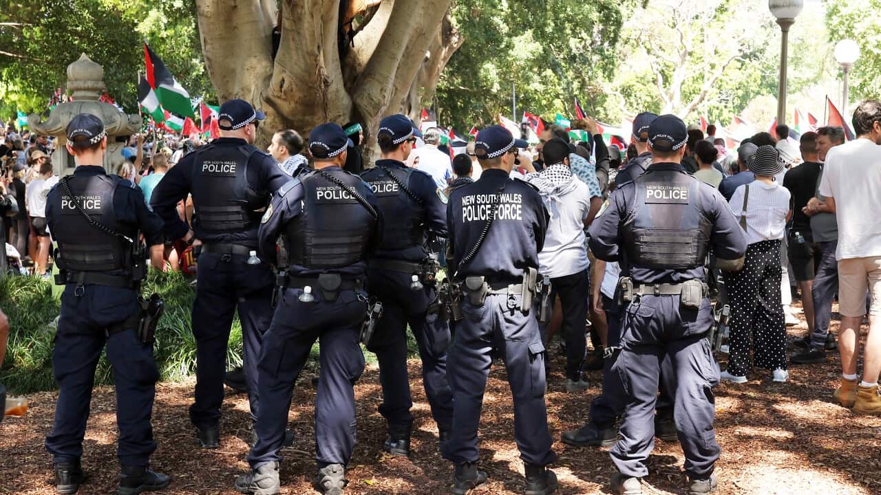 A group of NSW Police stand near protesters holding Palestinian flags at a demonstration.