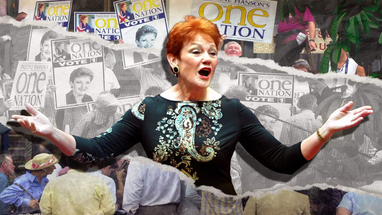 A woman speaking, arms stretched out. With vote One Nation posters in the background.