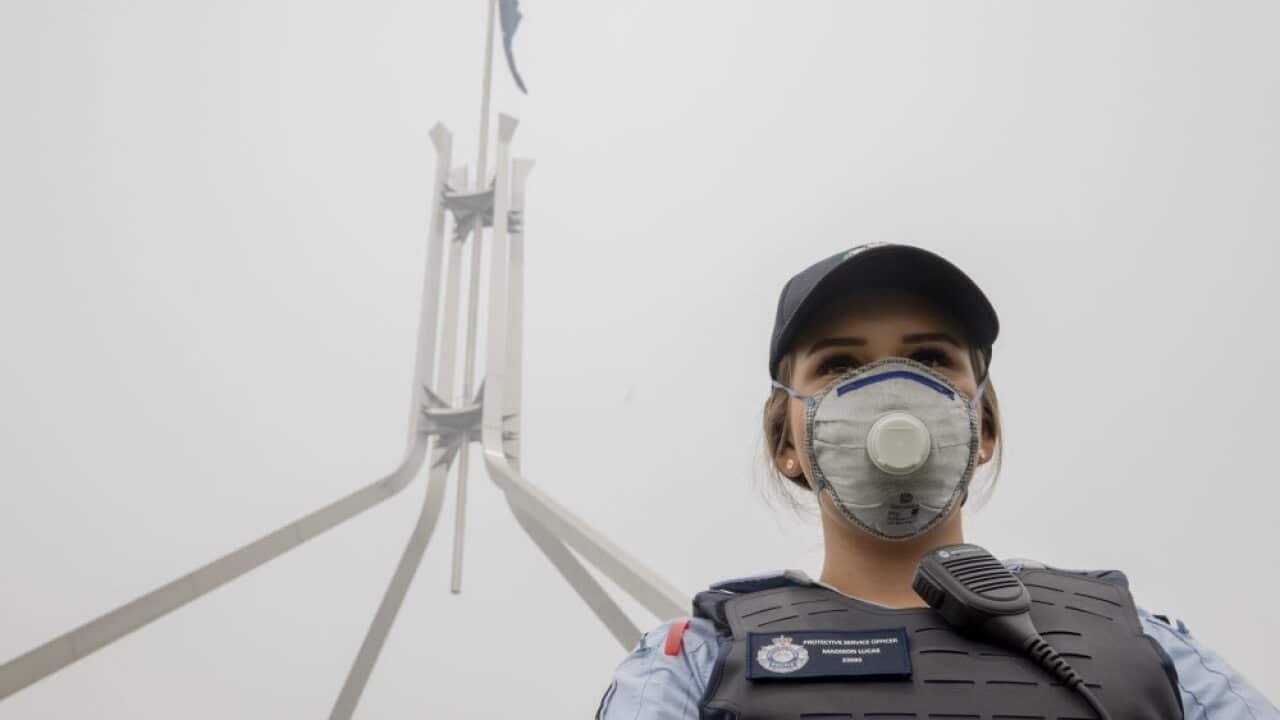 A police officer wears a protection mask while guarding in front of the flag mast on the Parliament House in Canberra