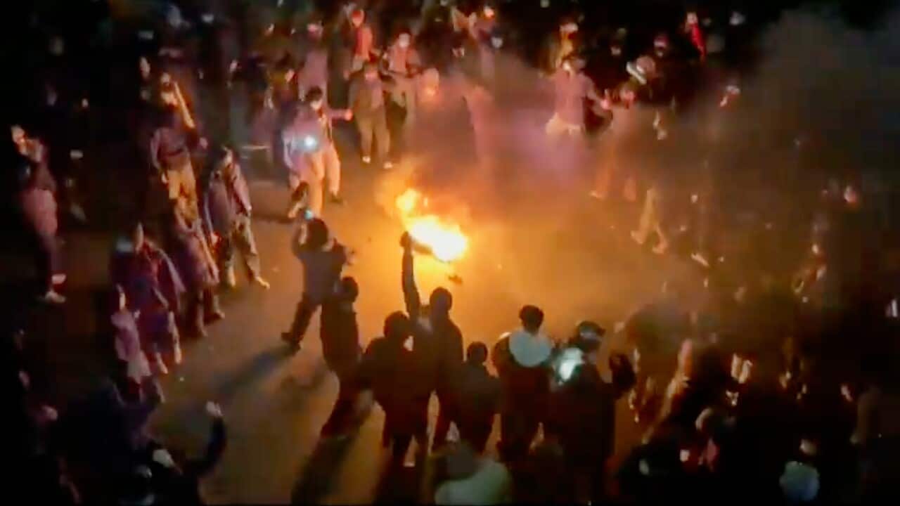 Protesters dancing and cheering around a bonfire on a street.