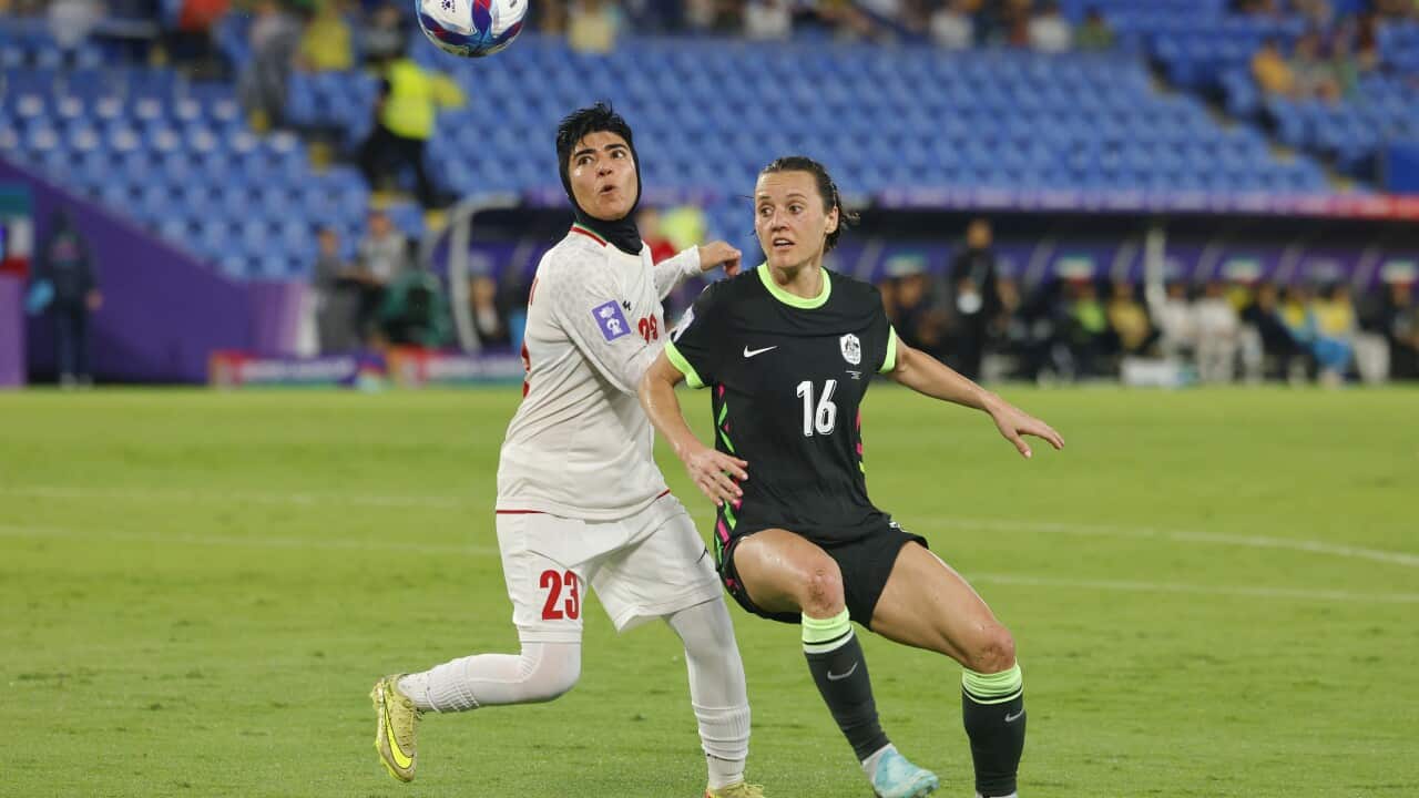 A woman in a white soccer uniform with a woman in a black soccer uniform going for the same ball