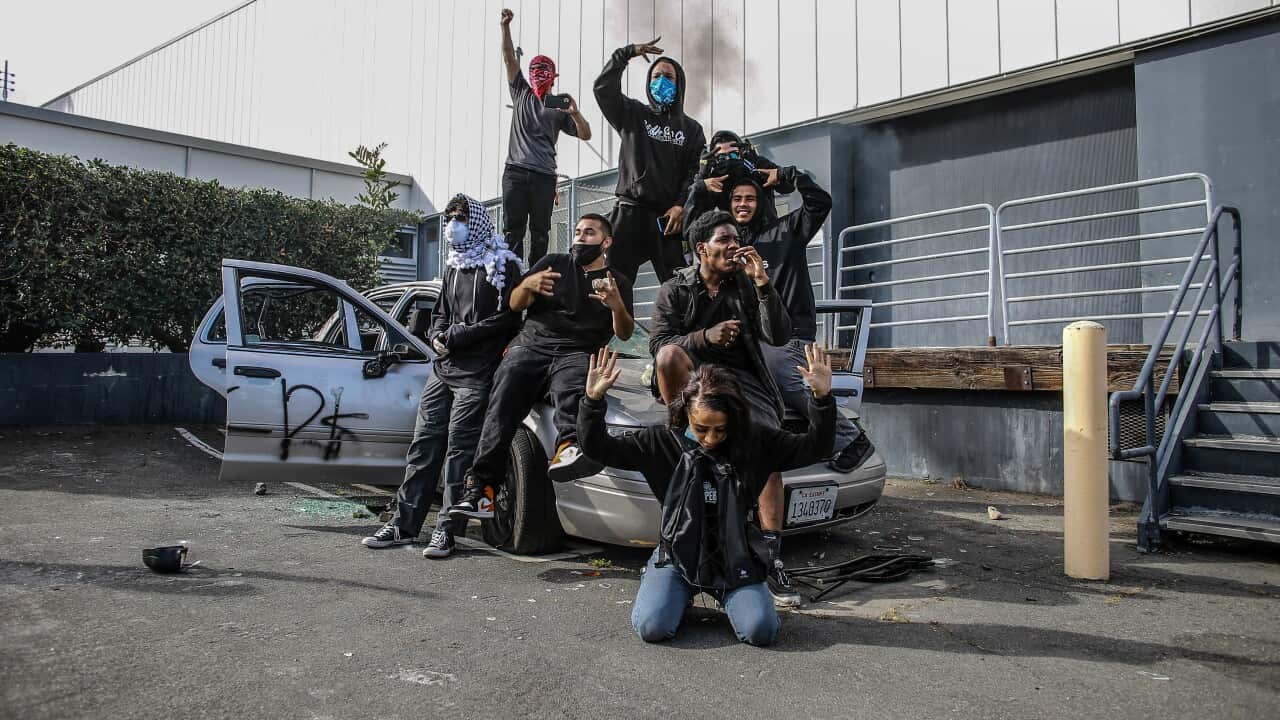 Protesters pose for a photograph on top of a destroyed car before setting it on fire during a protest in LA.