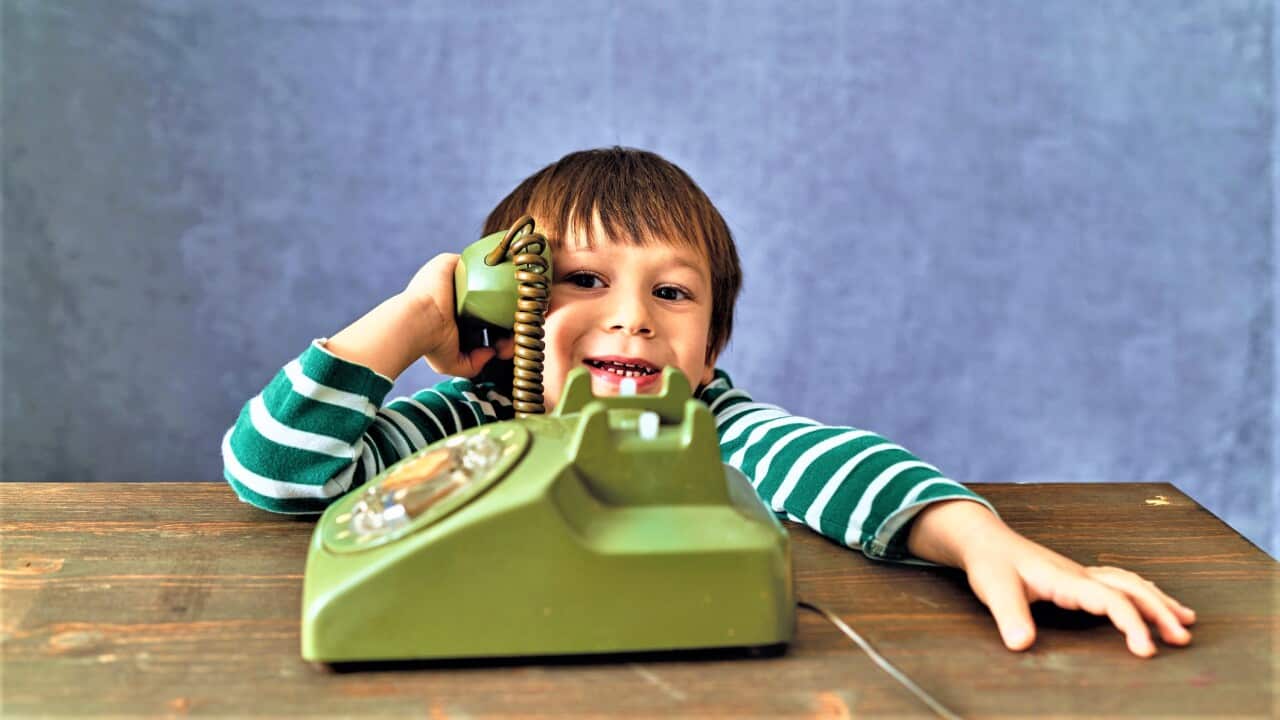 A kid talking via an old-fashioned phone.