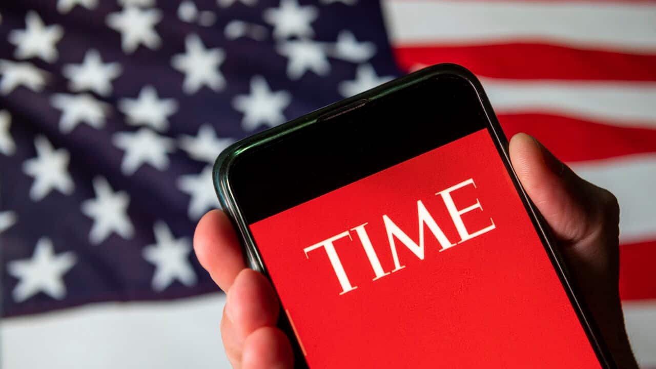 The Time magazine logo on a red background on a phone screen with the American flag behind it.